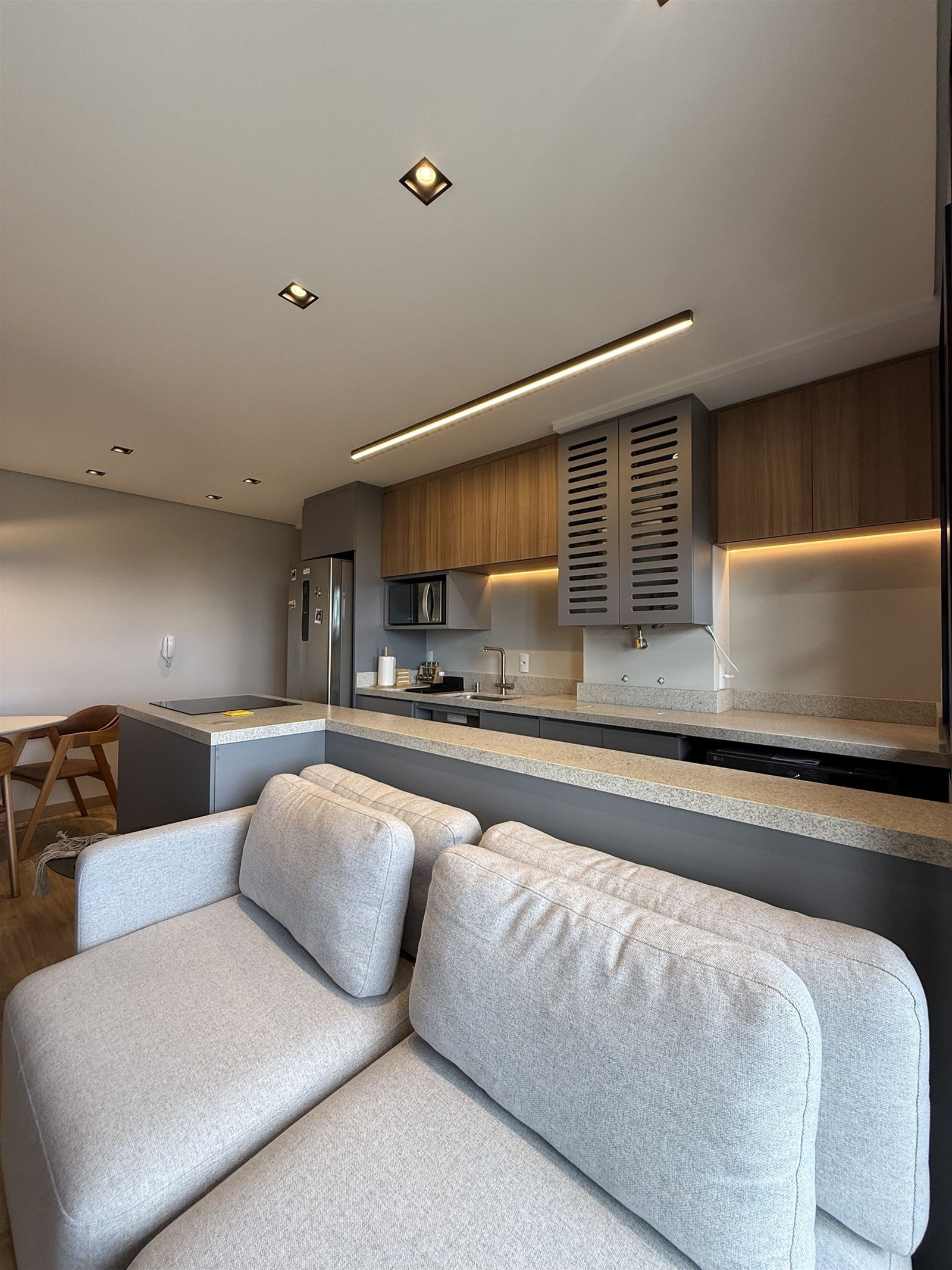 Sala de estar e cozinha integradas do Apartamento N+R, sofá cinza e marcenaria em tons neutros