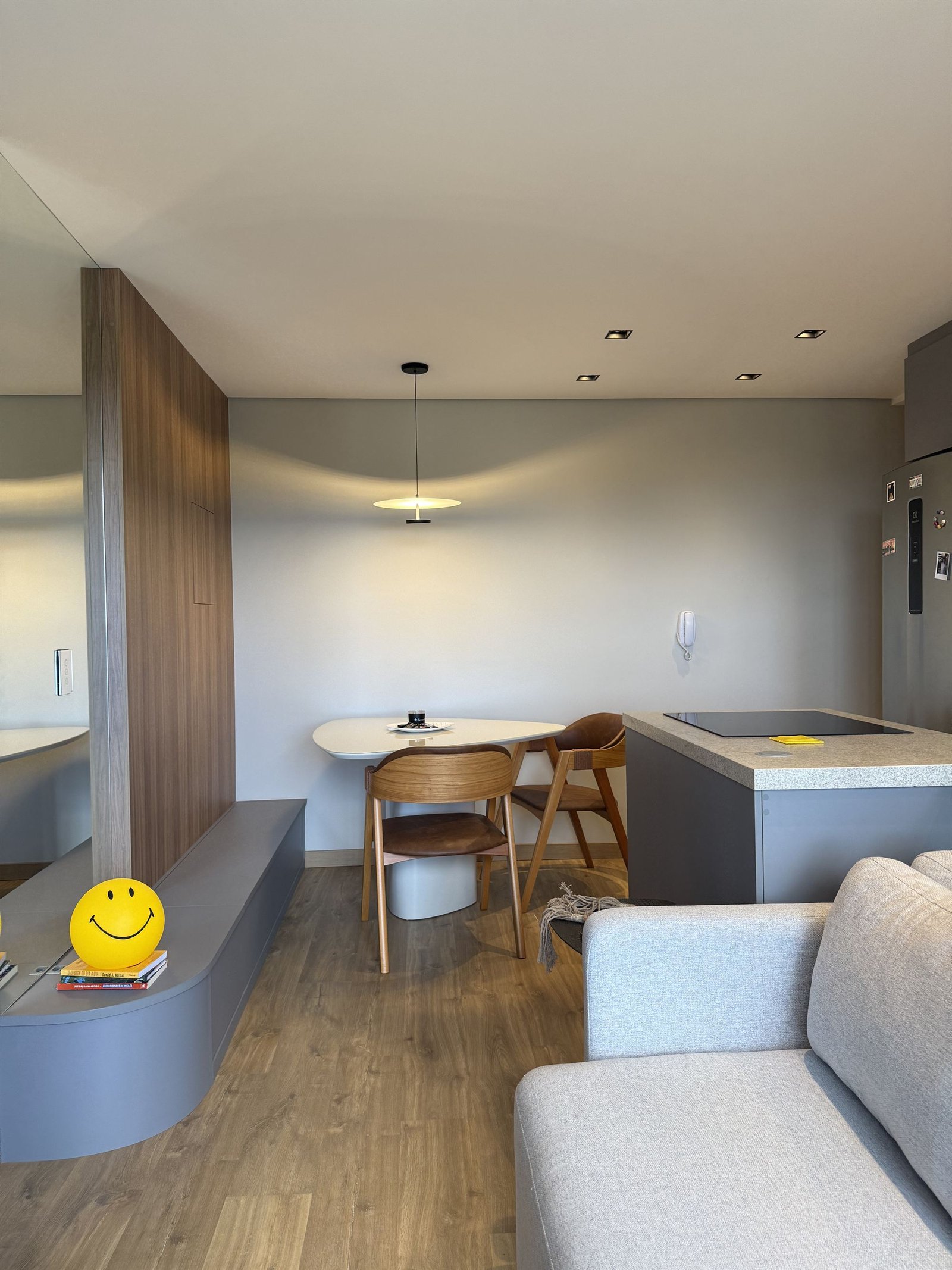 Sala de estar com a luminária smile amarela sobre o rack, mesa de jantar e cozinha ao fundo