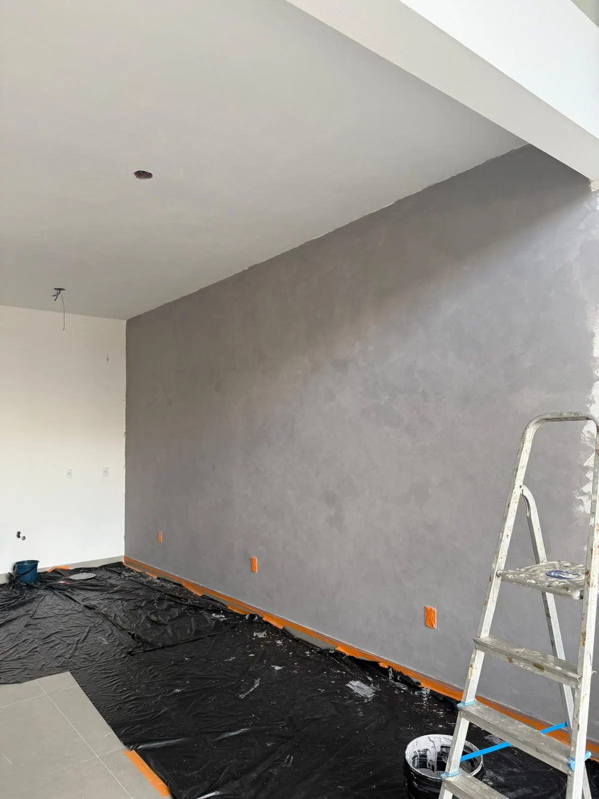 Parede sendo texturizada durante a obra, com escada e lona de proteção no chão