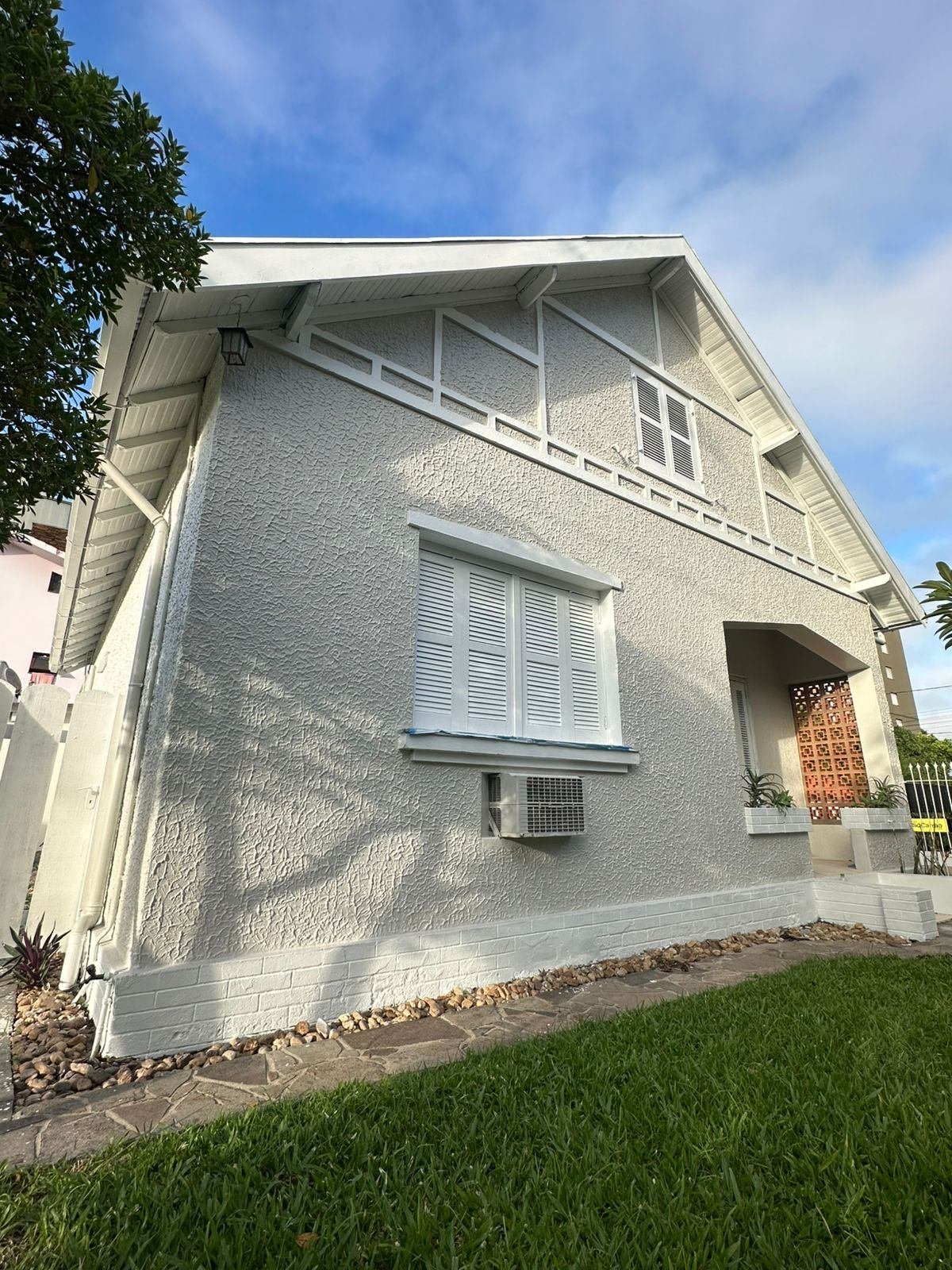 Fachada lateral da casa já repintada em branco e cinza-claro, com cobogó de concreto na entrada
