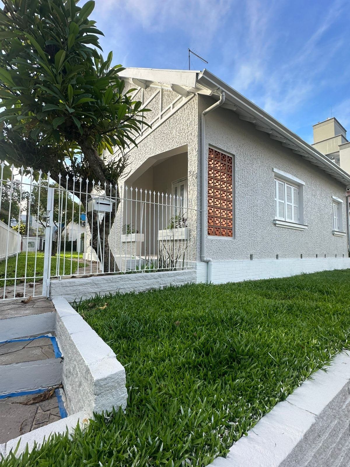 Outro ângulo da fachada repintada, com árvore e grades brancas