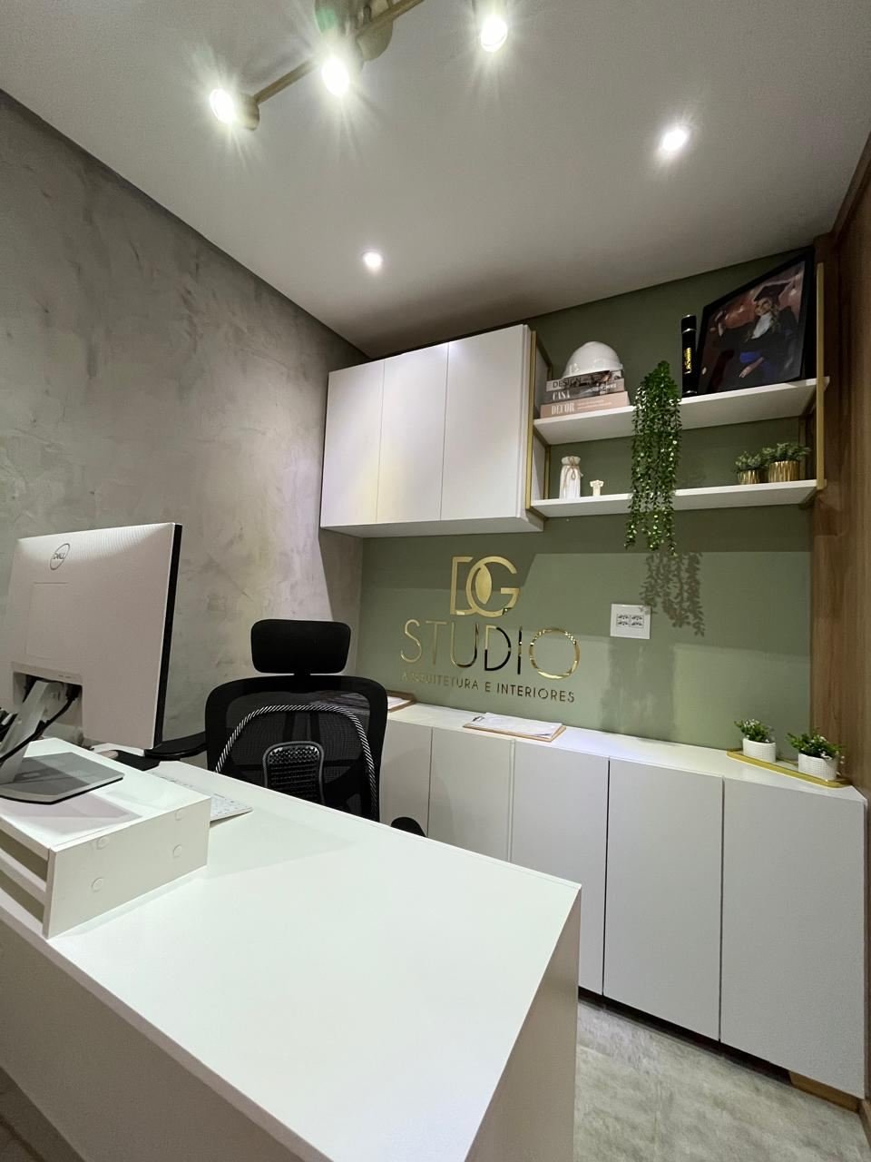 Parede assinada DG Studio, em verde-sálvia, com prateleiras e estante douradas