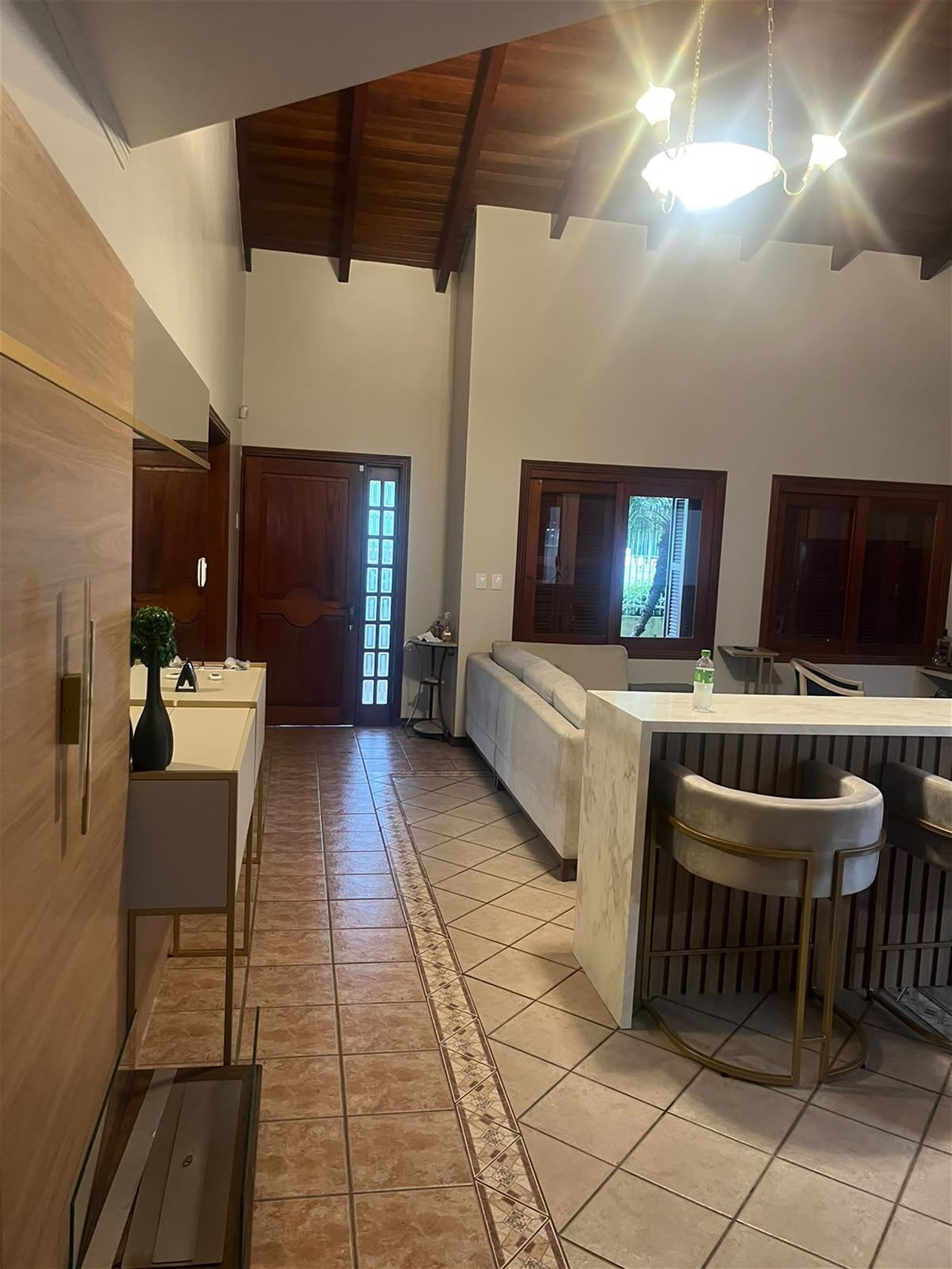 Sala de estar reconstruída, com bar em madeira, banquetas em veludo e teto em telhado aparente